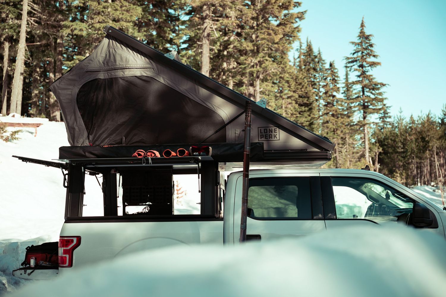 A black rooftop tent mounted on a vehicle in a snowy forest setting with evergreen trees in the background.