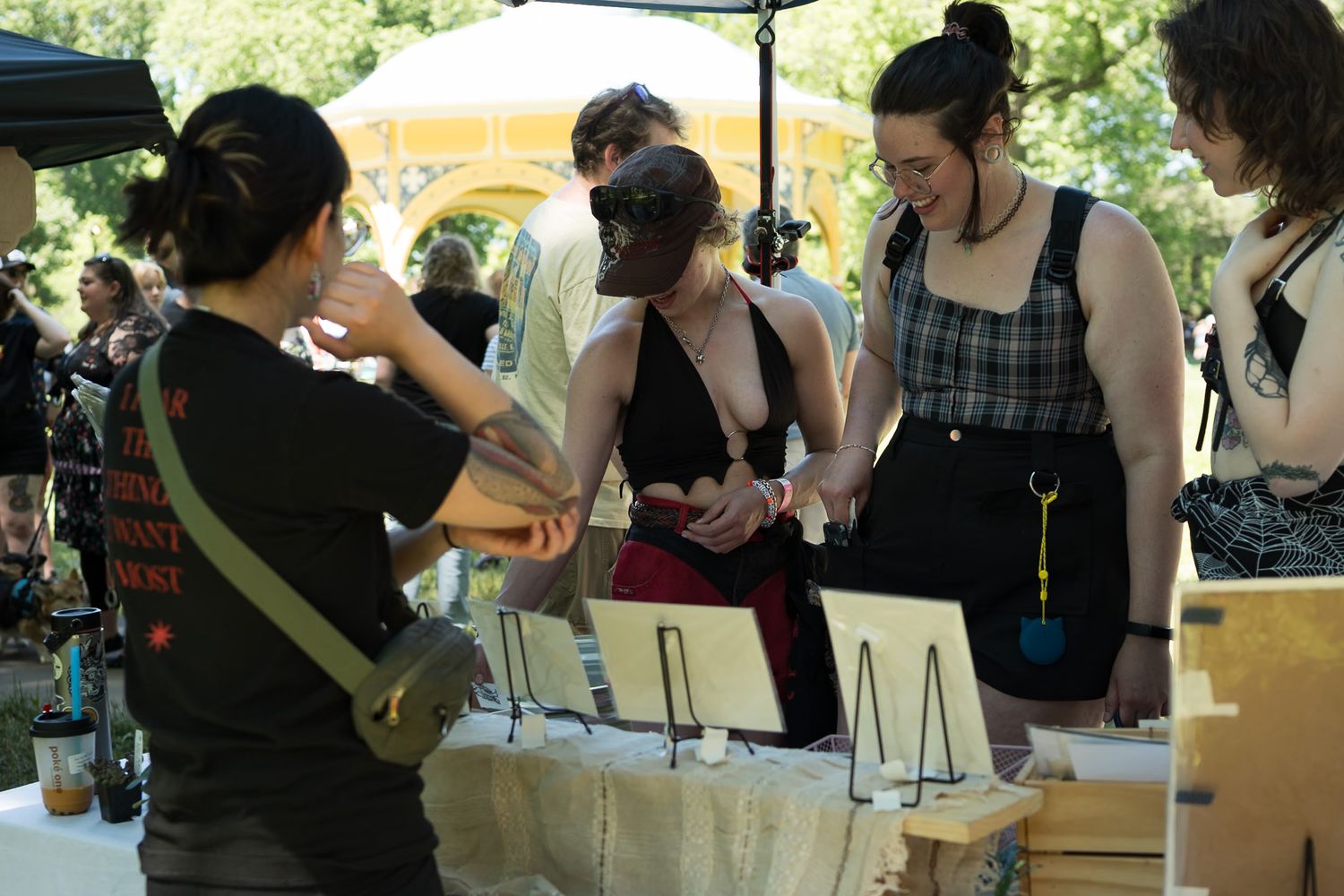 People browsing handmade wooden art pieces displayed on a table at an outdoor arts and crafts fair.