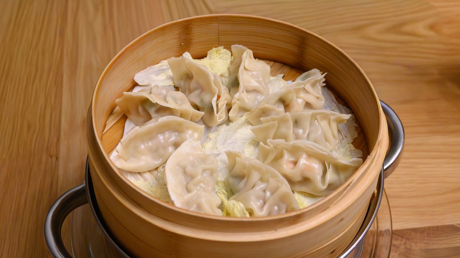 Freshly steamed dumplings served in a traditional bamboo steamer basket on a wooden surface.