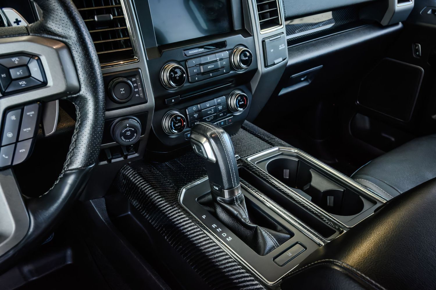 Ford F-150 interior showing automatic gear shifter, center console, dual cup holders, and dashboard controls.