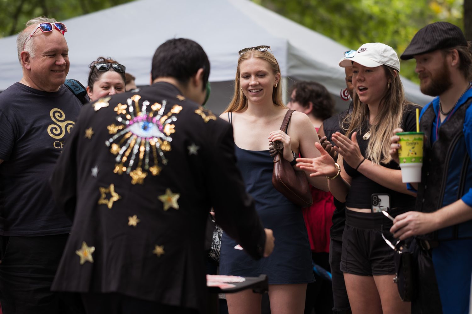 Group of people gathered outdoors at a festival, smiling and interacting in a park setting.