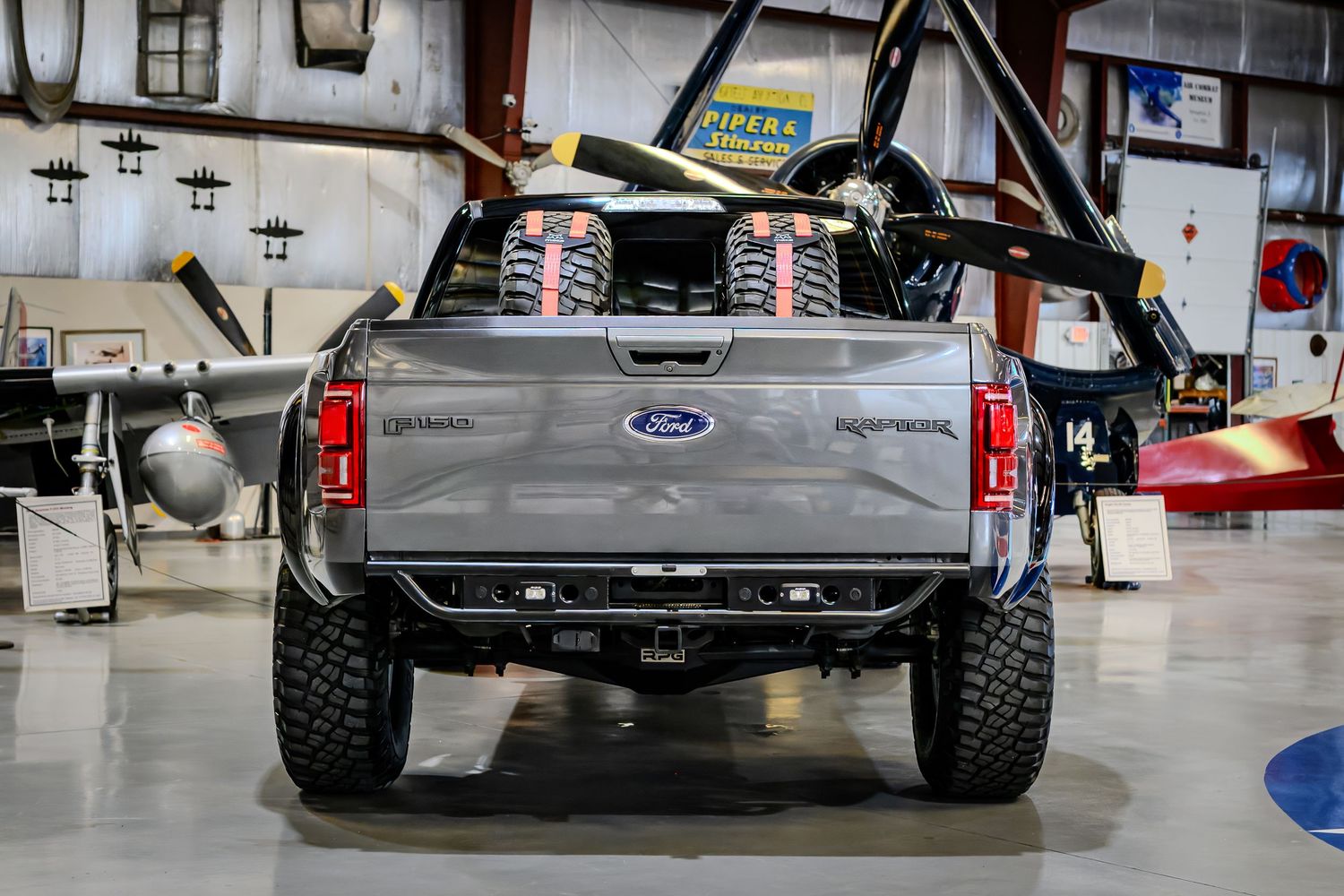 Rear view of a modified Ford F-150 Raptor with exposed suspension in a hangar.