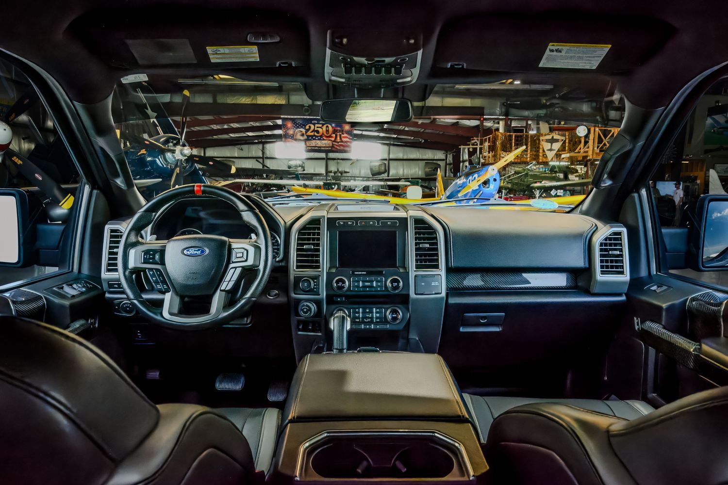 Interior view of a Ford F-150 truck cabin showing dashboard, infotainment screen, and leather seats in a factory setting.