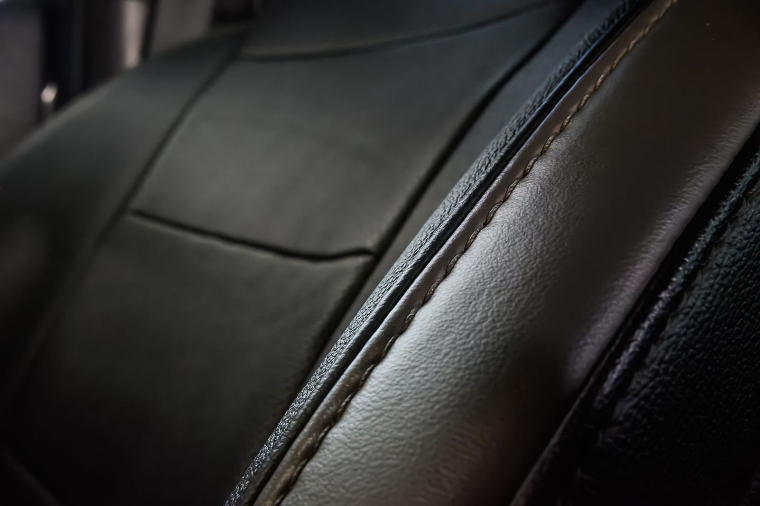 Close-up of black leather car seat with stitched seams and textured surface detail.