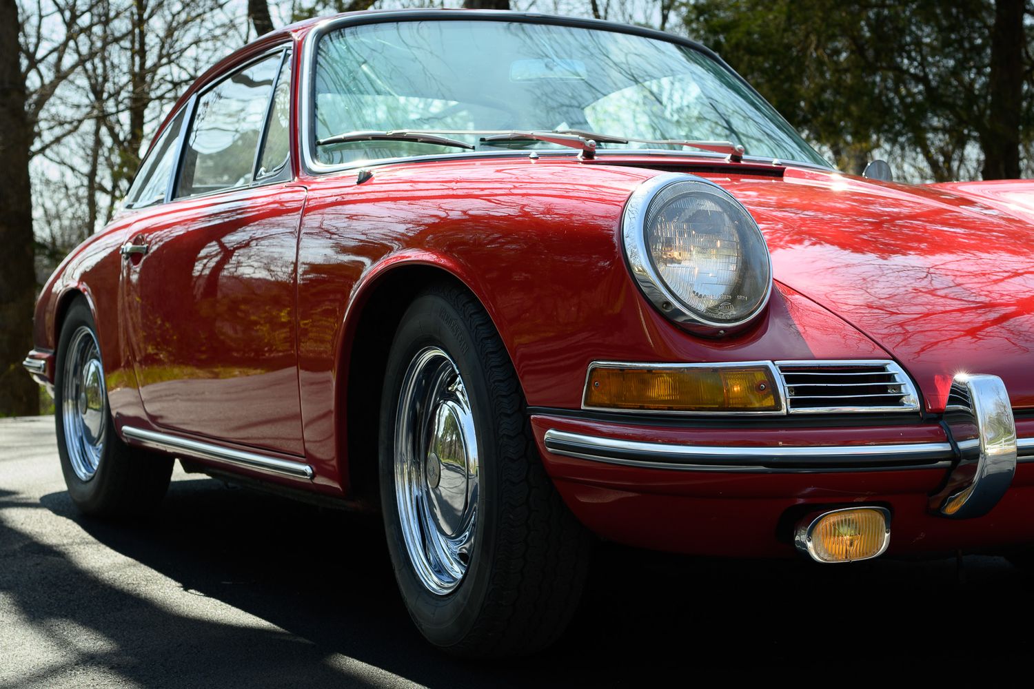 Close-up front detail of a vintage red Porsche 911 showing round headlight and chrome trim.