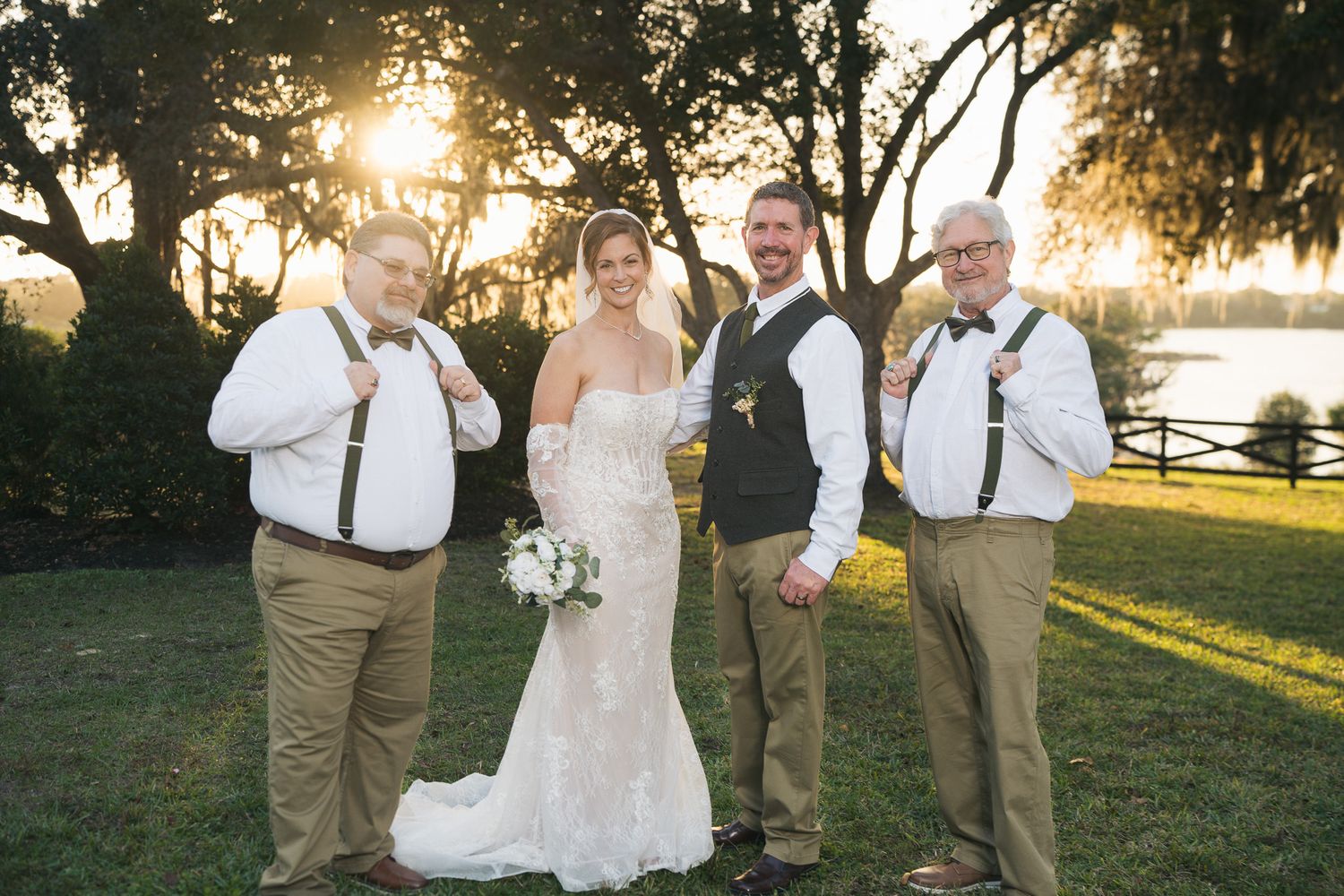 Bride and groom pose with groomsmen wearing suspenders and bow ties at sunset wedding.