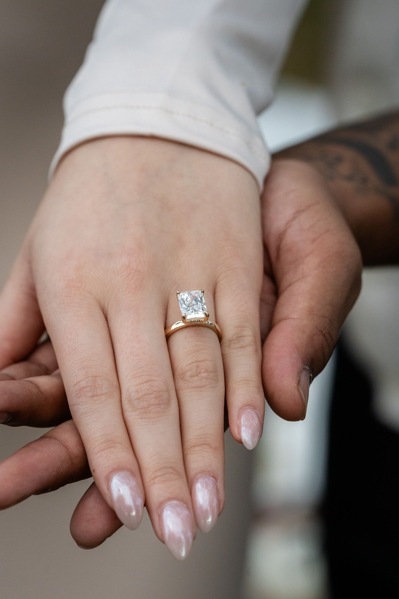 Close-up of a woman's hand displaying a large radiant-cut diamond engagement ring in gold.