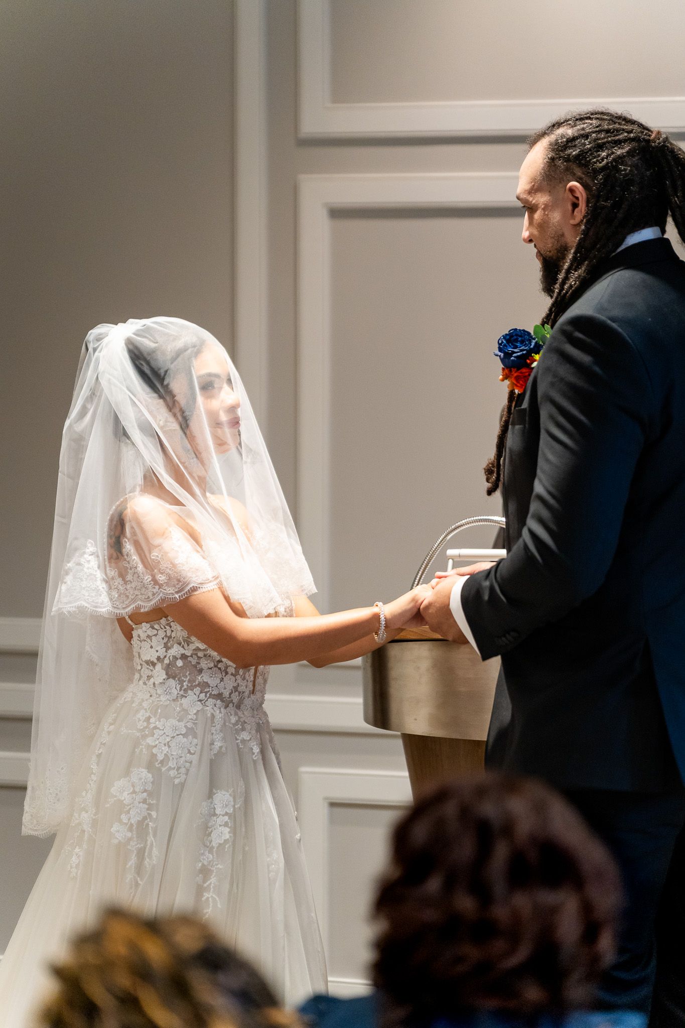 Bride and groom hold hands at altar during emotional indoor wedding ceremony with veil detail.