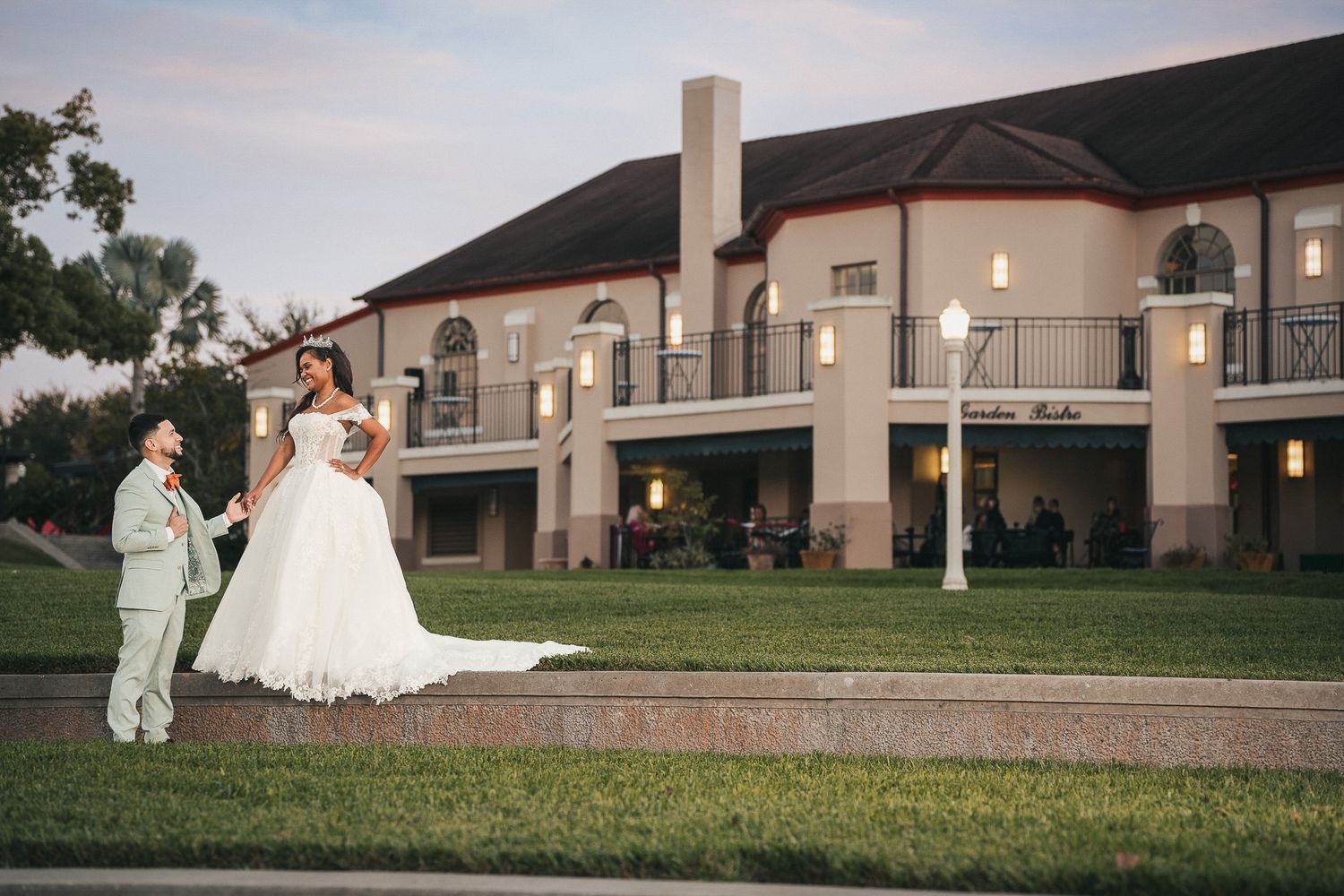Bride in large white ballgown and groom in suit posing outside elegant wedding venue at dusk.