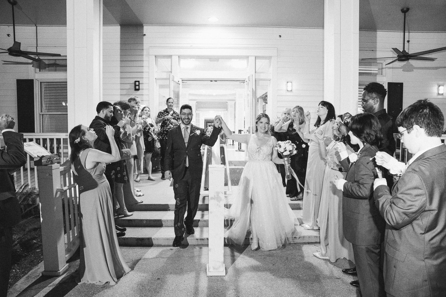 Black and white photo of bride and groom exiting through celebrating wedding guests at night.