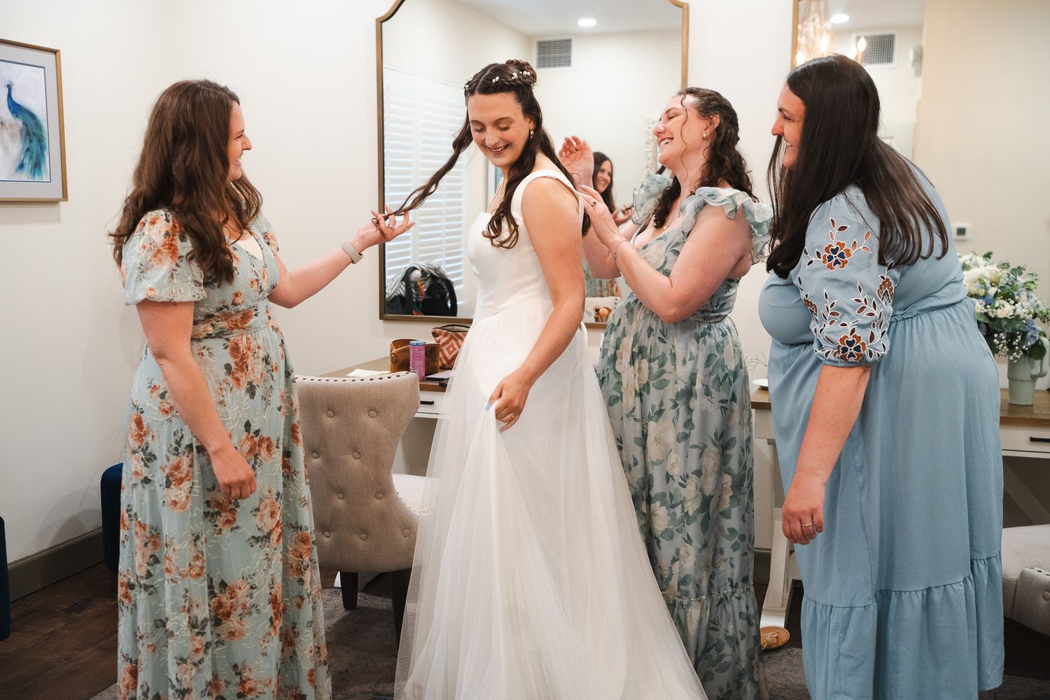Bride in white wedding gown laughing with three bridesmaids in floral dresses.
