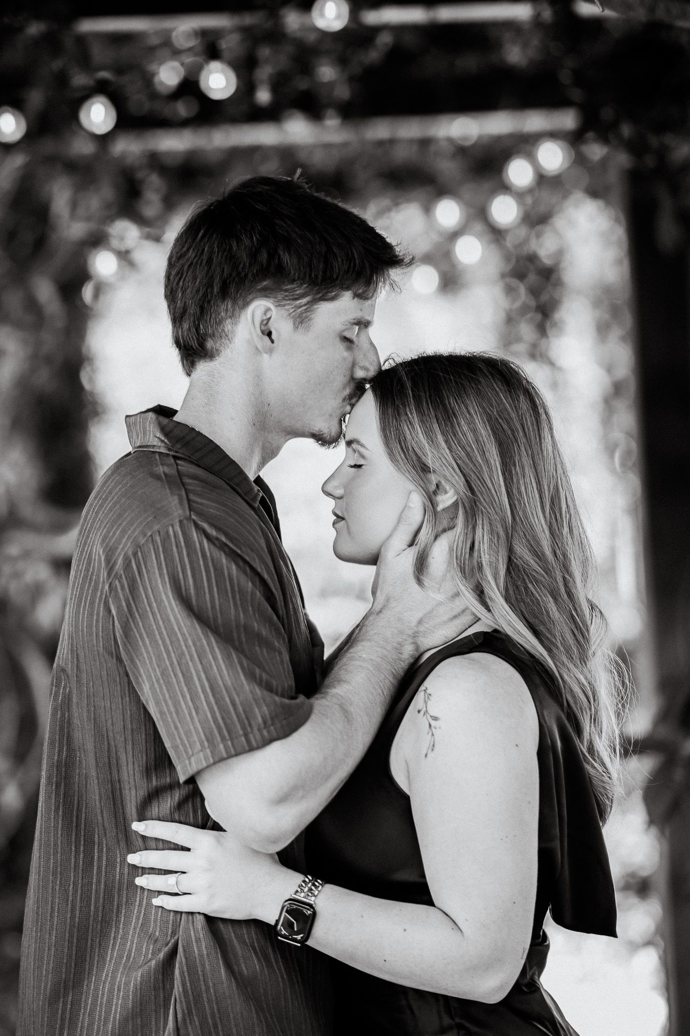 Black and white photo of a romantic couple sharing an intimate moment, man gently holding womans face as they lean in to kiss.