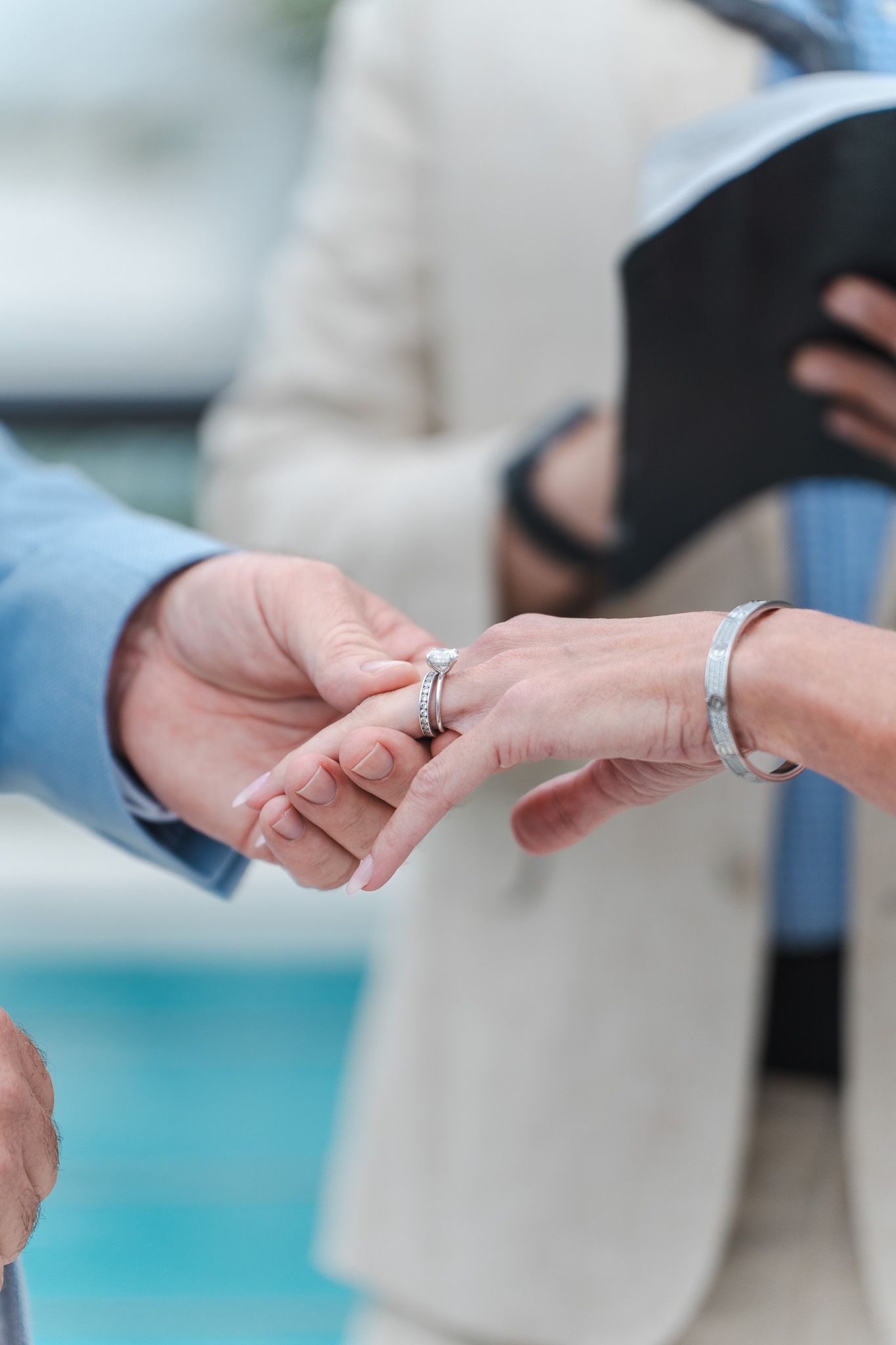 Close-up of groom placing wedding ring on brides finger during outdoor wedding ceremony.