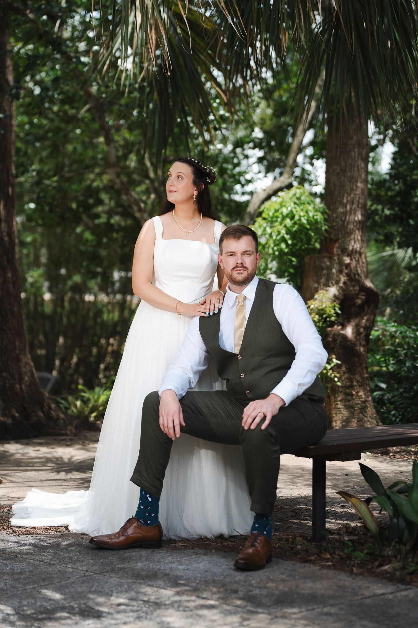 Bride and groom pose together on bench surrounded by lush tropical greenery.