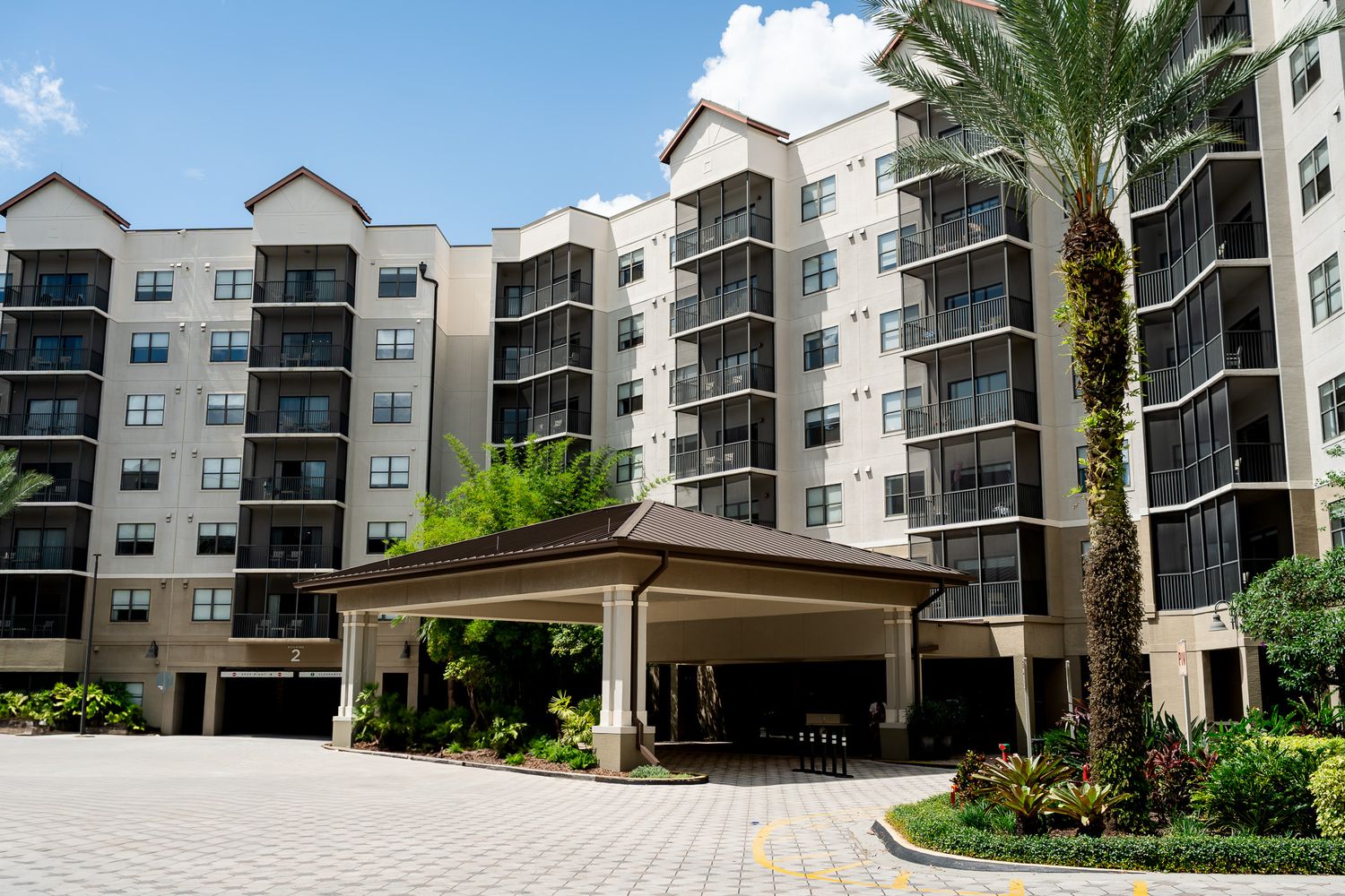 Grand hotel exterior with palm trees, covered valet entrance, and paved driveway.