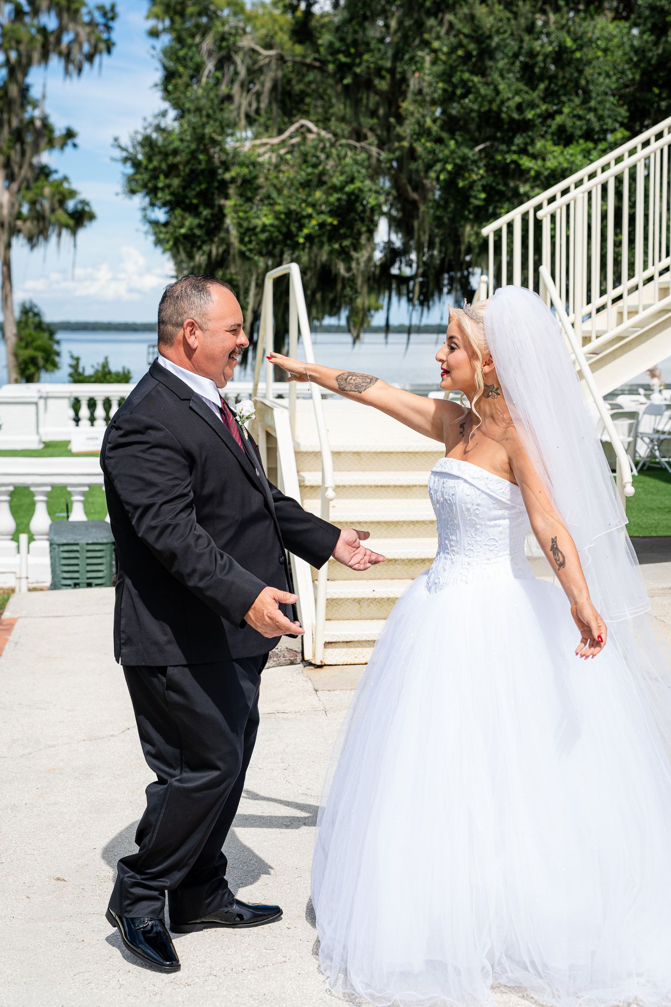 Bride in white tulle gown and groom in black suit share joyful first look by waterfront.
