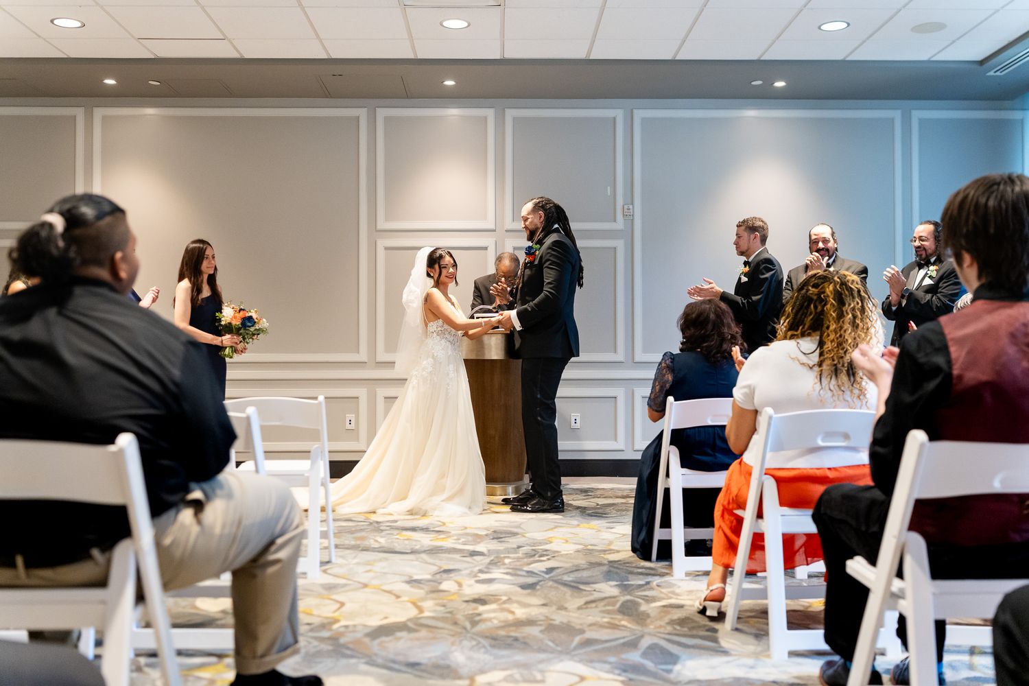 Intimate indoor wedding ceremony with small group of seated guests applauding.