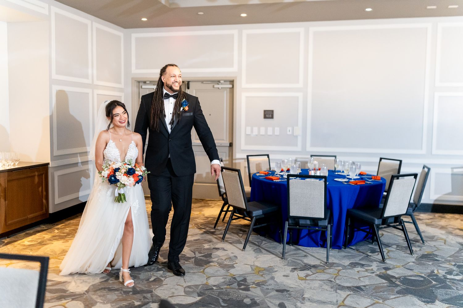 Elegant couple walks into wedding reception with royal blue table settings and floral centerpieces.