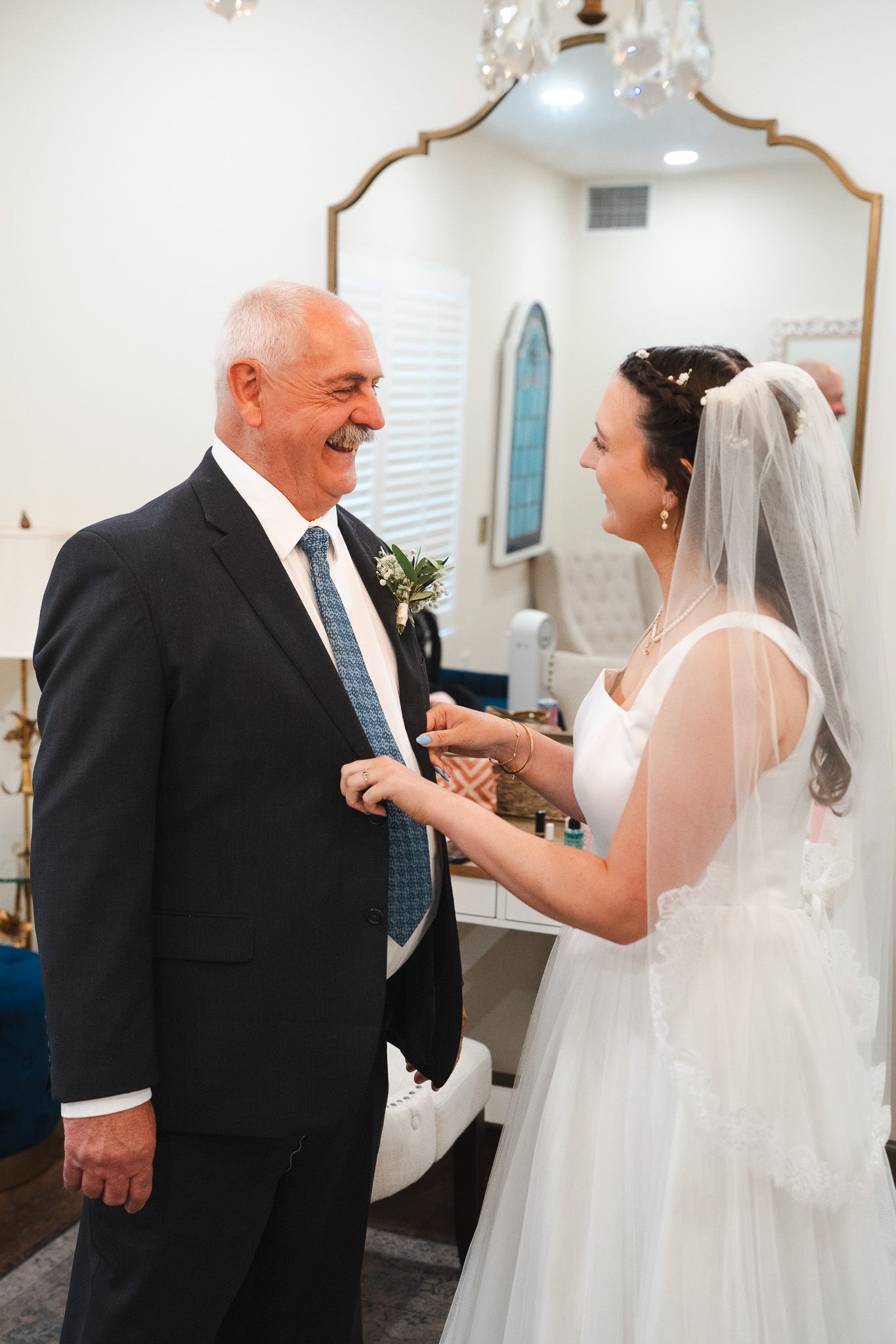 Smiling bride in white gown and veil sharing a moment with her father.