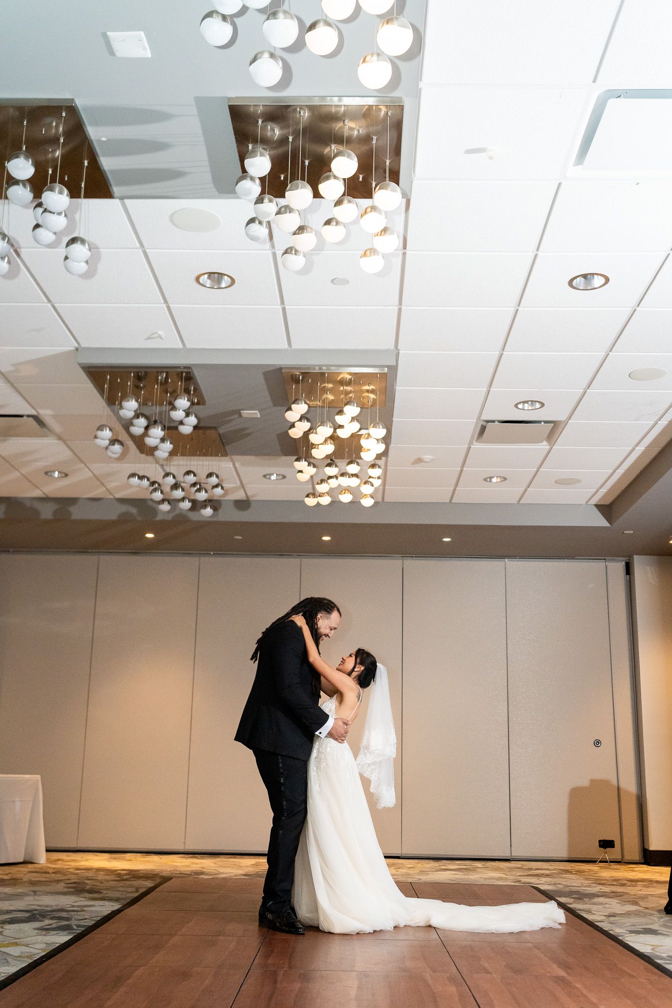 Bride and groom share first dance under sparkling globe chandeliers in elegant ballroom.