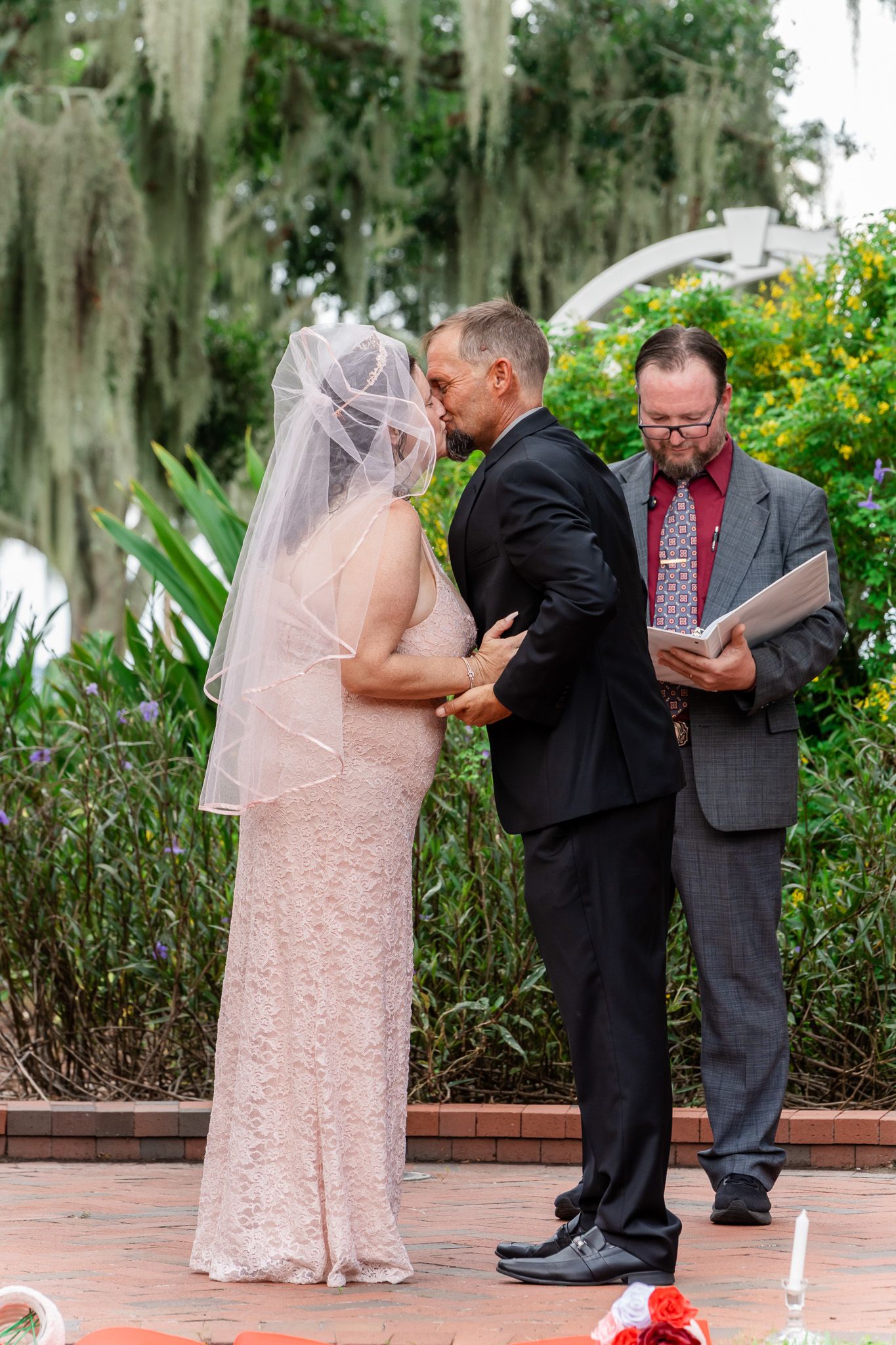 Bride and groom exchange vows outdoors at a wedding ceremony with an officiant reading from a book.