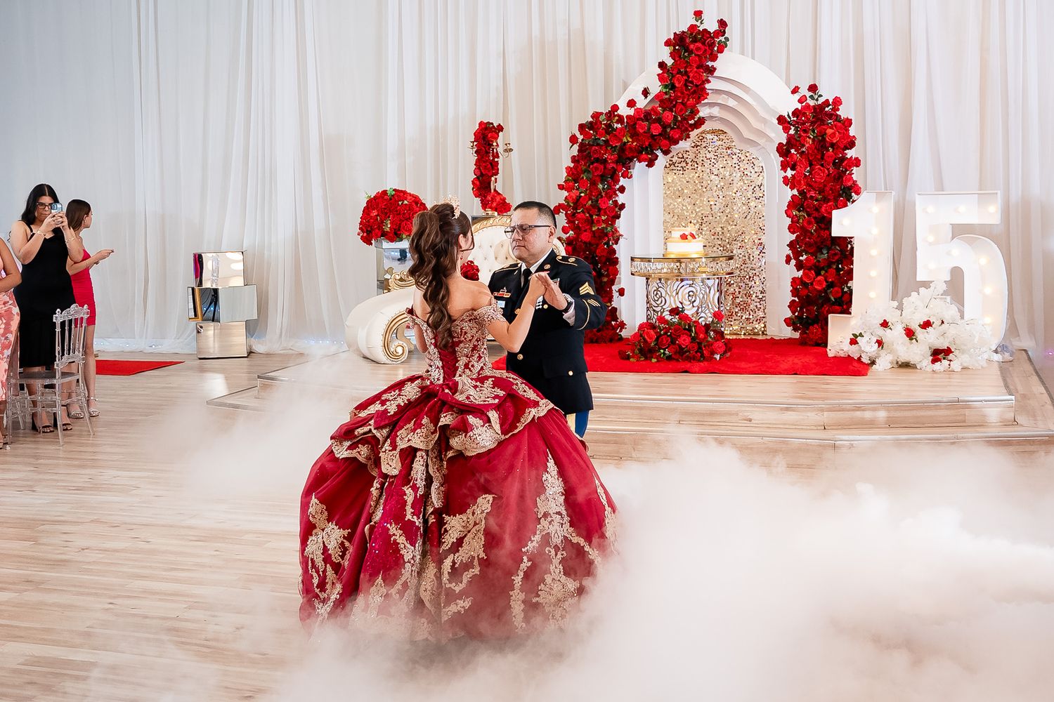 Quinceañera girl in red gold ballgown dances in fog with escort at elegant 15th birthday party.