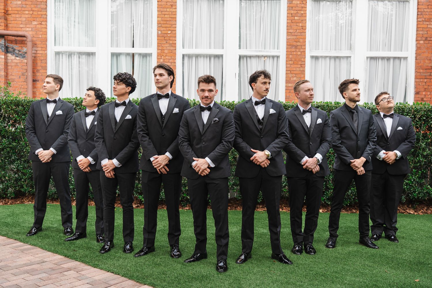 Groom and groomsmen in matching black tuxedos posing outdoors on green lawn.