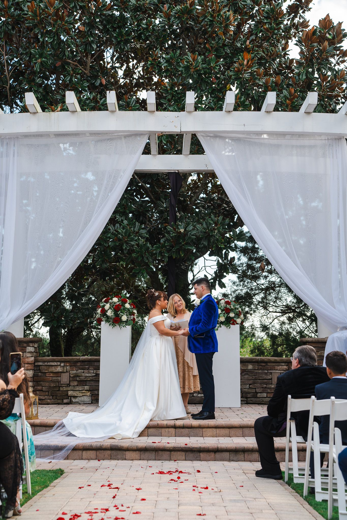 Bride and groom exchange vows under white draped pergola at outdoor garden wedding ceremony.