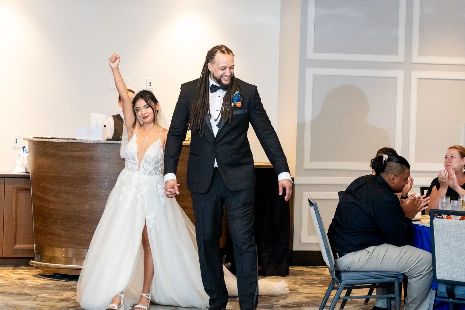 Bride and groom make grand entrance into wedding reception hall with arm raised in celebration.