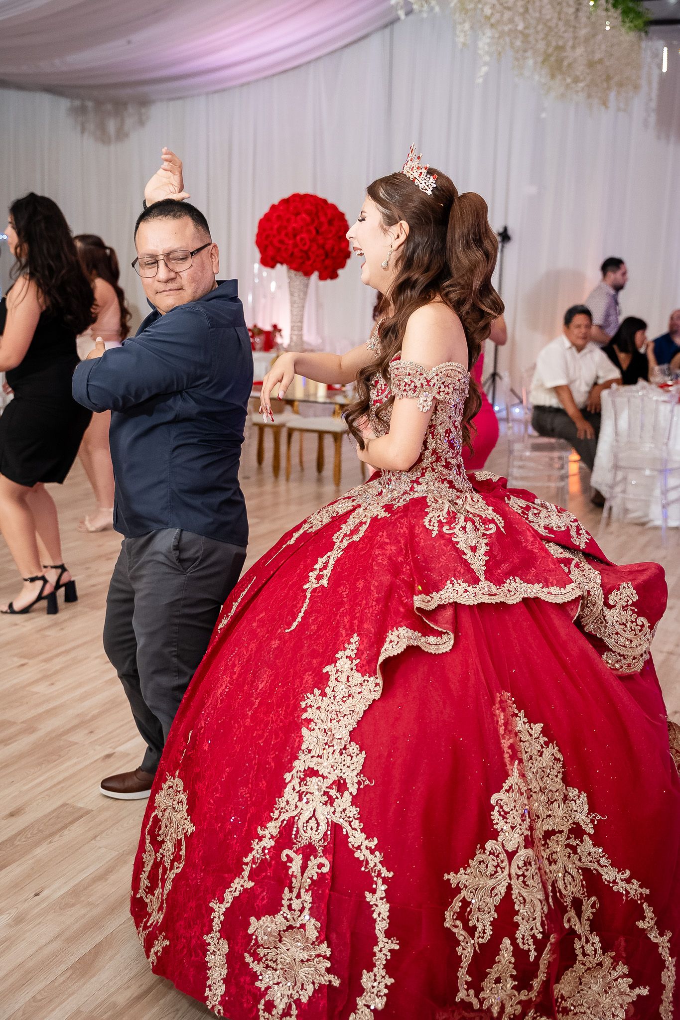 Young woman in red quinceañera ball gown dances with man in navy suit at elegant party celebration.