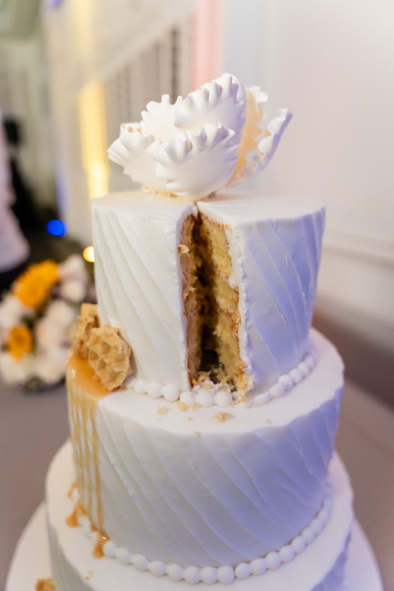 Close-up of a sliced three-tier white wedding cake with gold drip accents and a floral topper.