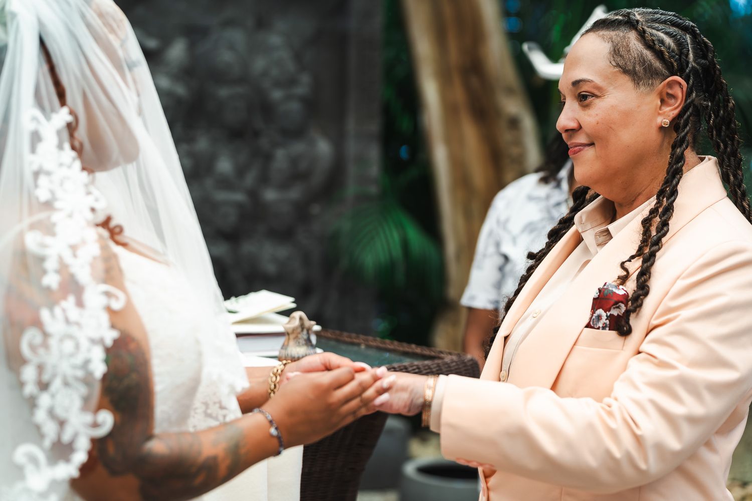 Bride in peach suit holds hands with bride in lace gown during intimate wedding ceremony.