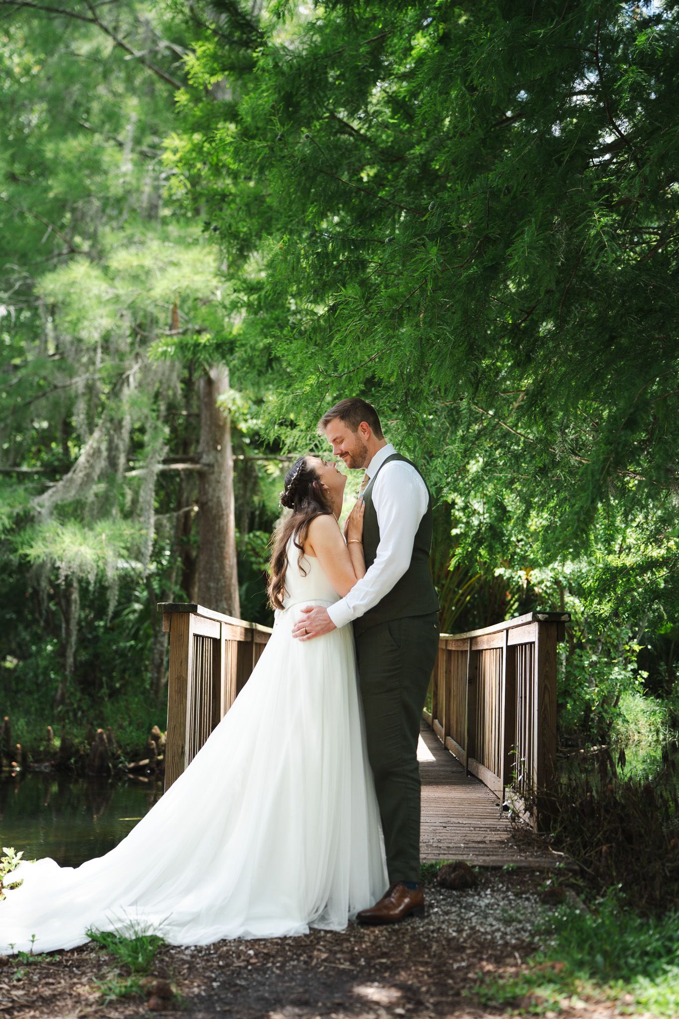 Bride and groom share an intimate moment on a wooden bridge surrounded by moss-draped trees.