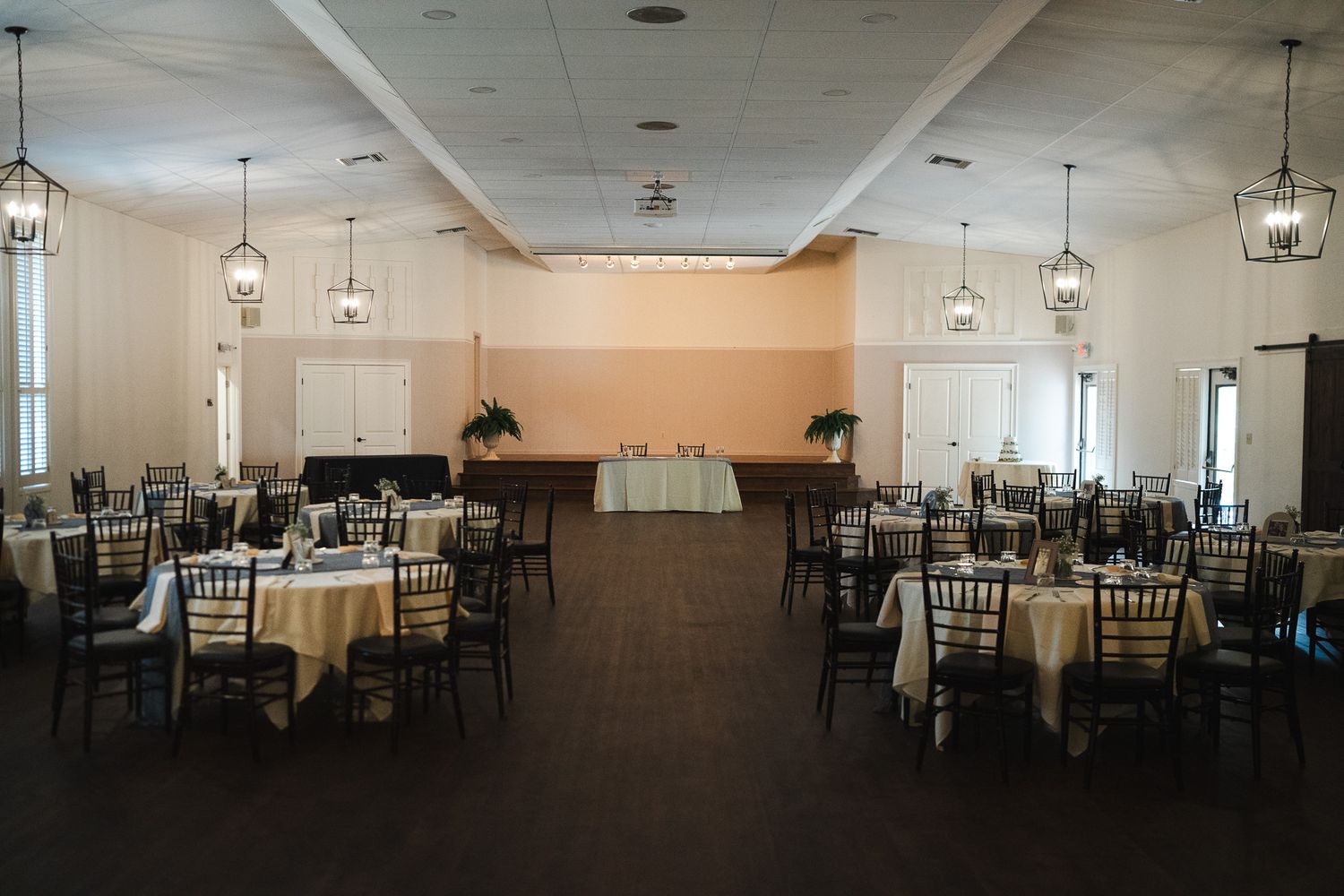 Spacious wedding reception ballroom with round tables, chiavari chairs, and pendant lighting.