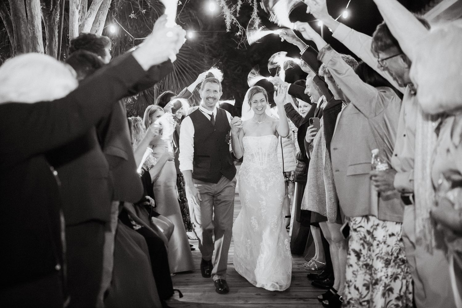 Bride and groom exit wedding ceremony through sparkler send-off in black and white photo.