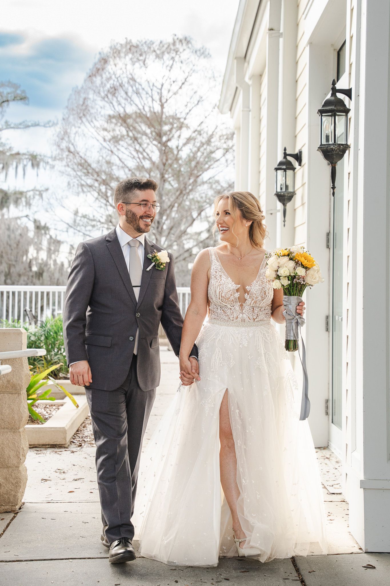 Bride and groom walk hand in hand outside elegant white wedding venue.