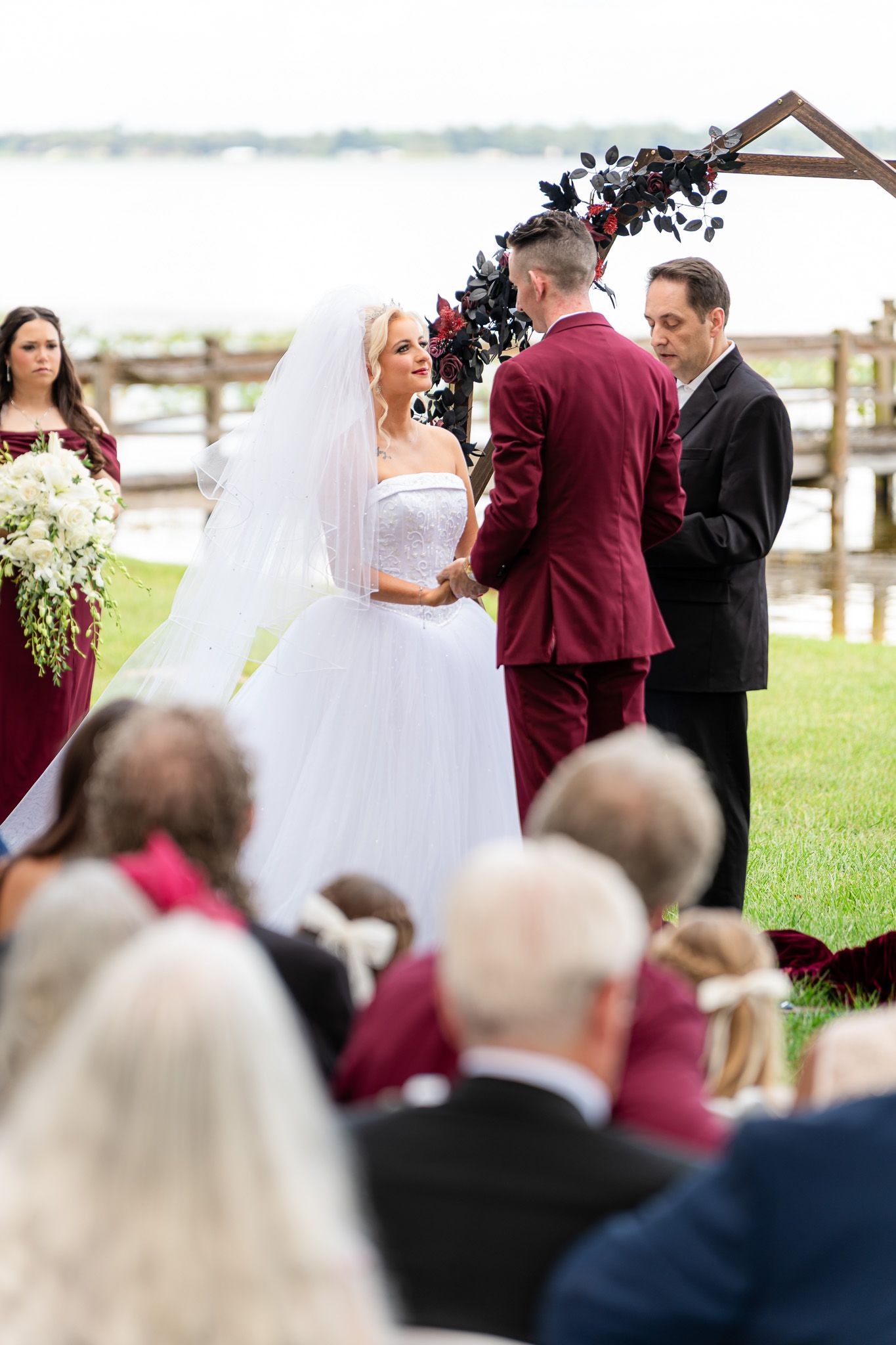 Bride and groom exchange vows at outdoor lakeside wedding ceremony with floral arch backdrop.