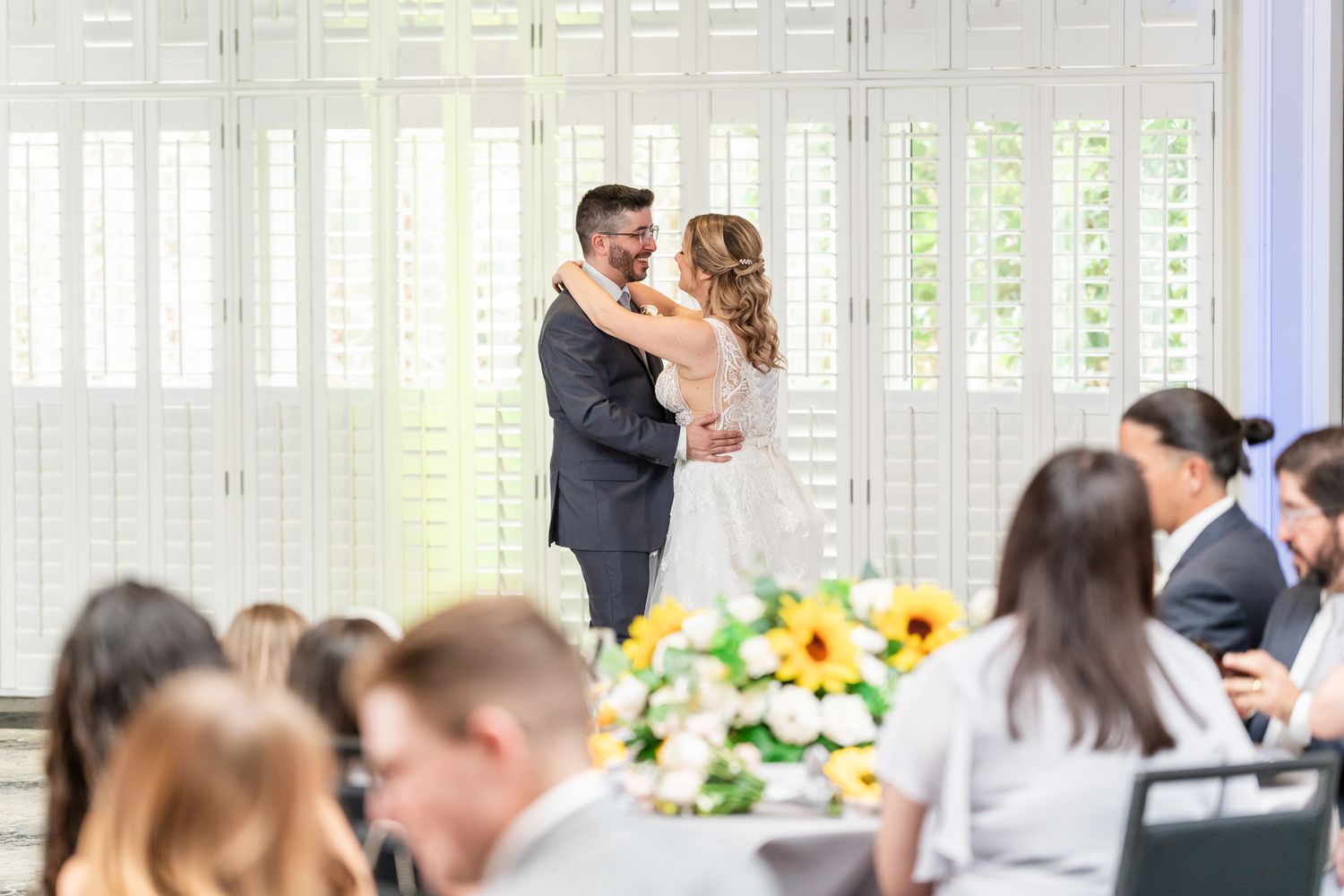 Bride and groom share first dance at elegant wedding reception with sunflower centerpieces.