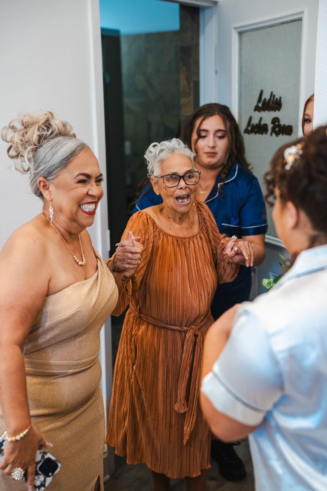 Joyful grandmother in orange dress reacts with excitement upon seeing bride on wedding day.