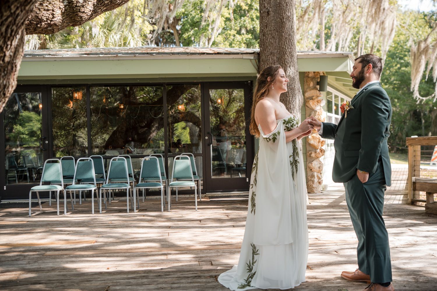 Bride and groom share a first look moment outdoors under oak trees with ceremony chairs in background.