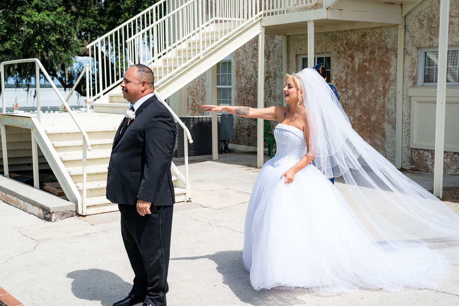 Bride in white ball gown and veil shares first look moment with groom in black suit outdoors.