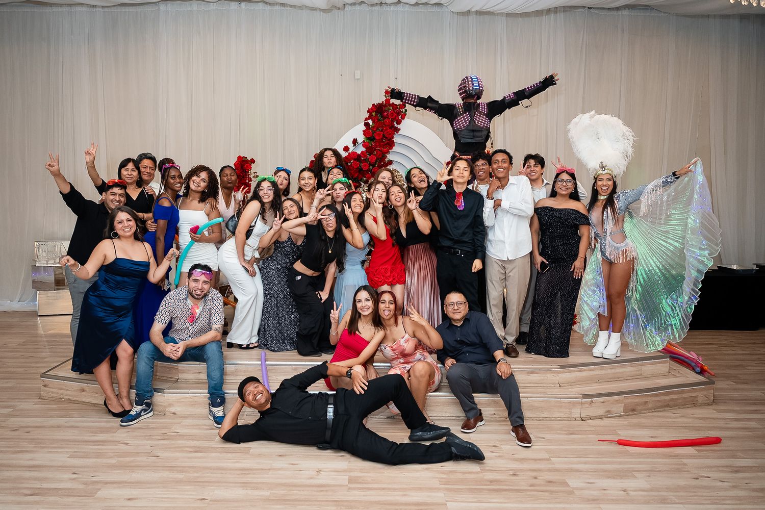 Large group of elegantly dressed people posing together at a formal event with dancers in colorful costumes.