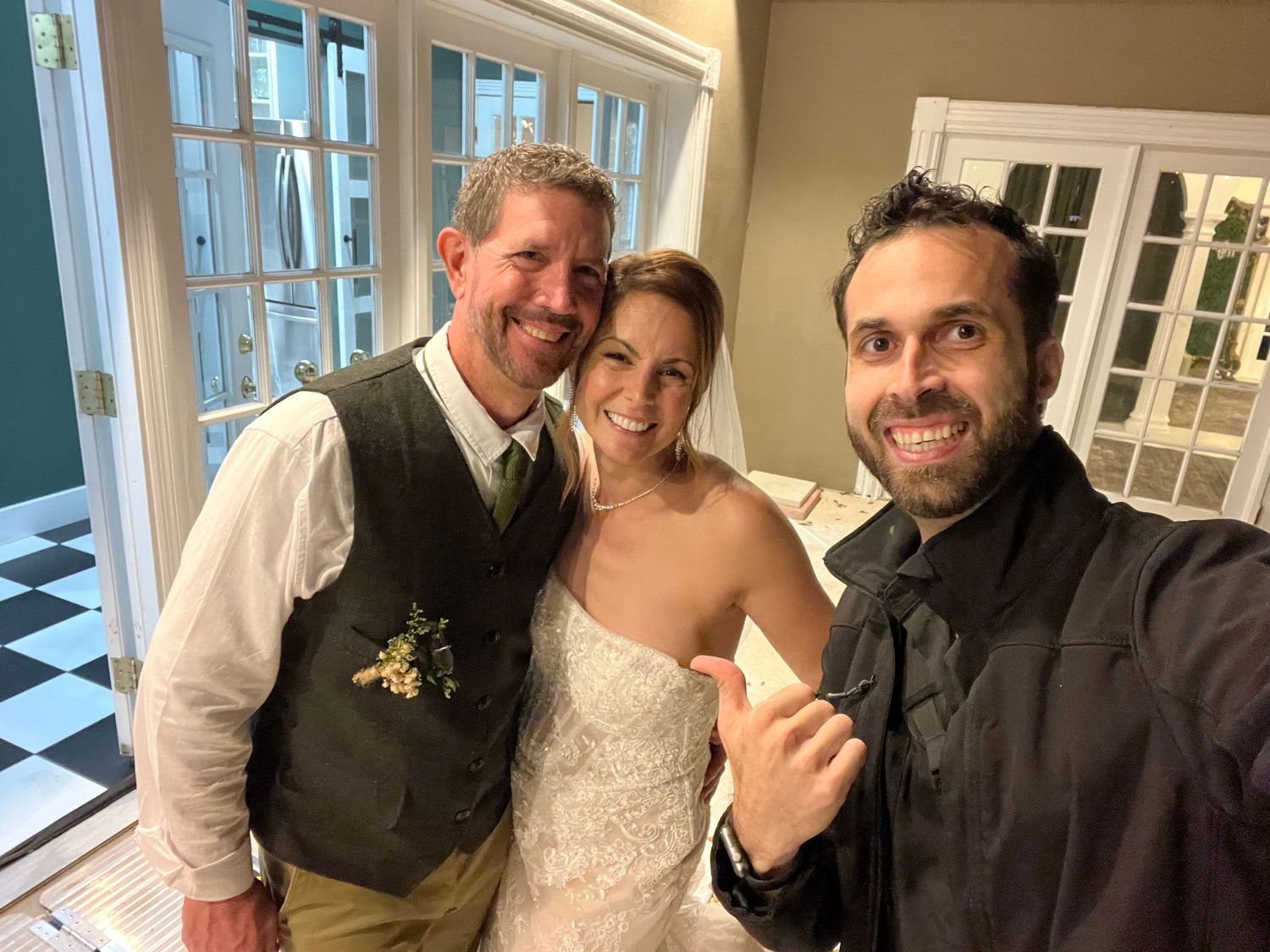 Wedding photographer posing with smiling bride and groom inside an elegant venue after the ceremony.