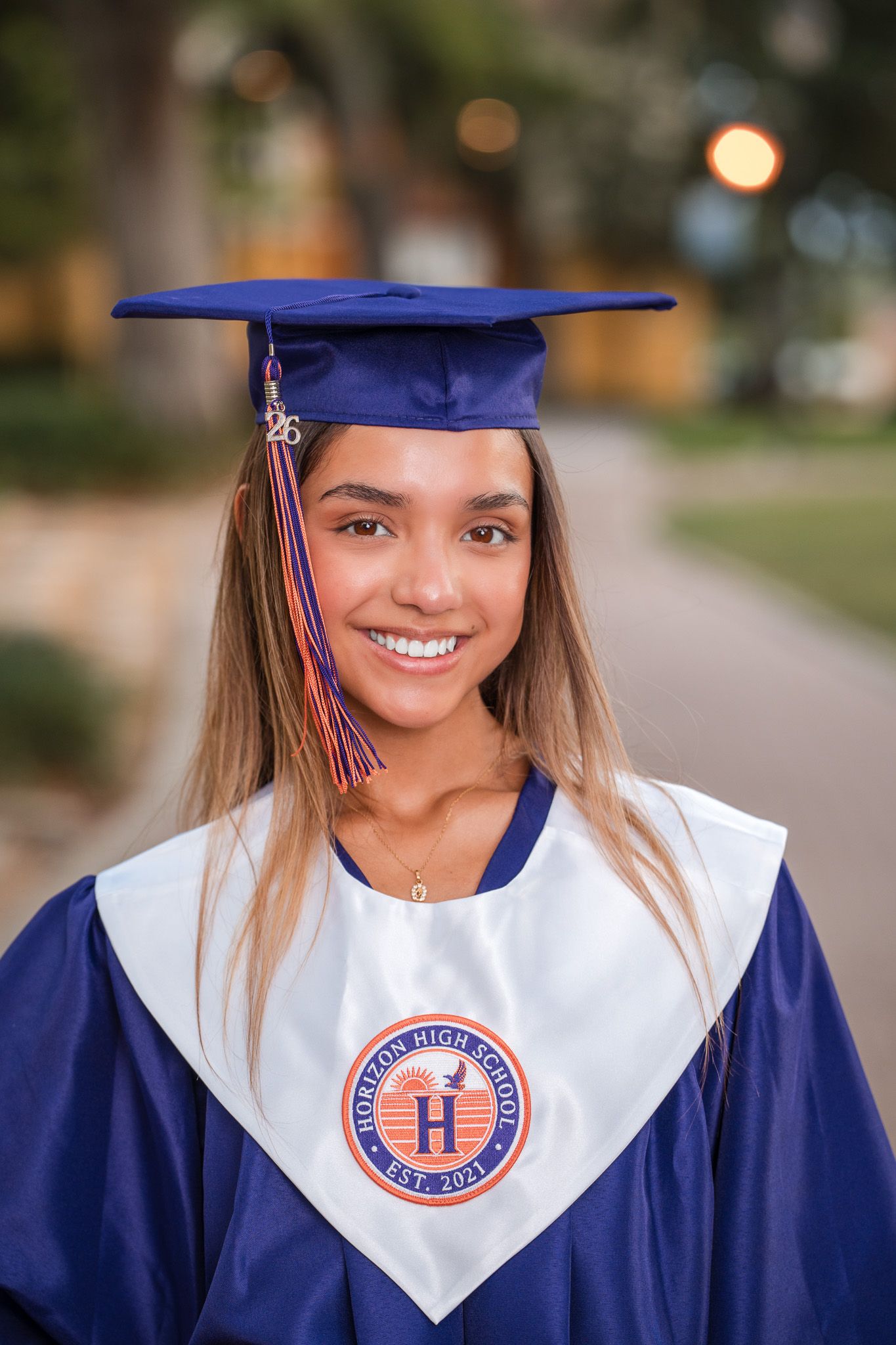 Young woman in blue graduation cap and gown from Horizon High School smiling outdoors.
