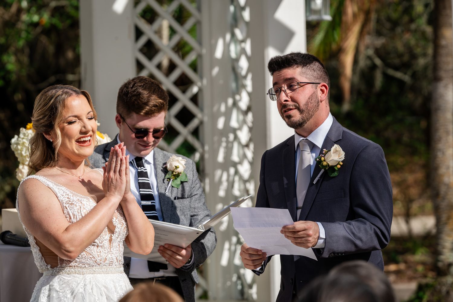 Bride and groom exchange heartfelt vows at an outdoor wedding ceremony beneath a white pergola.