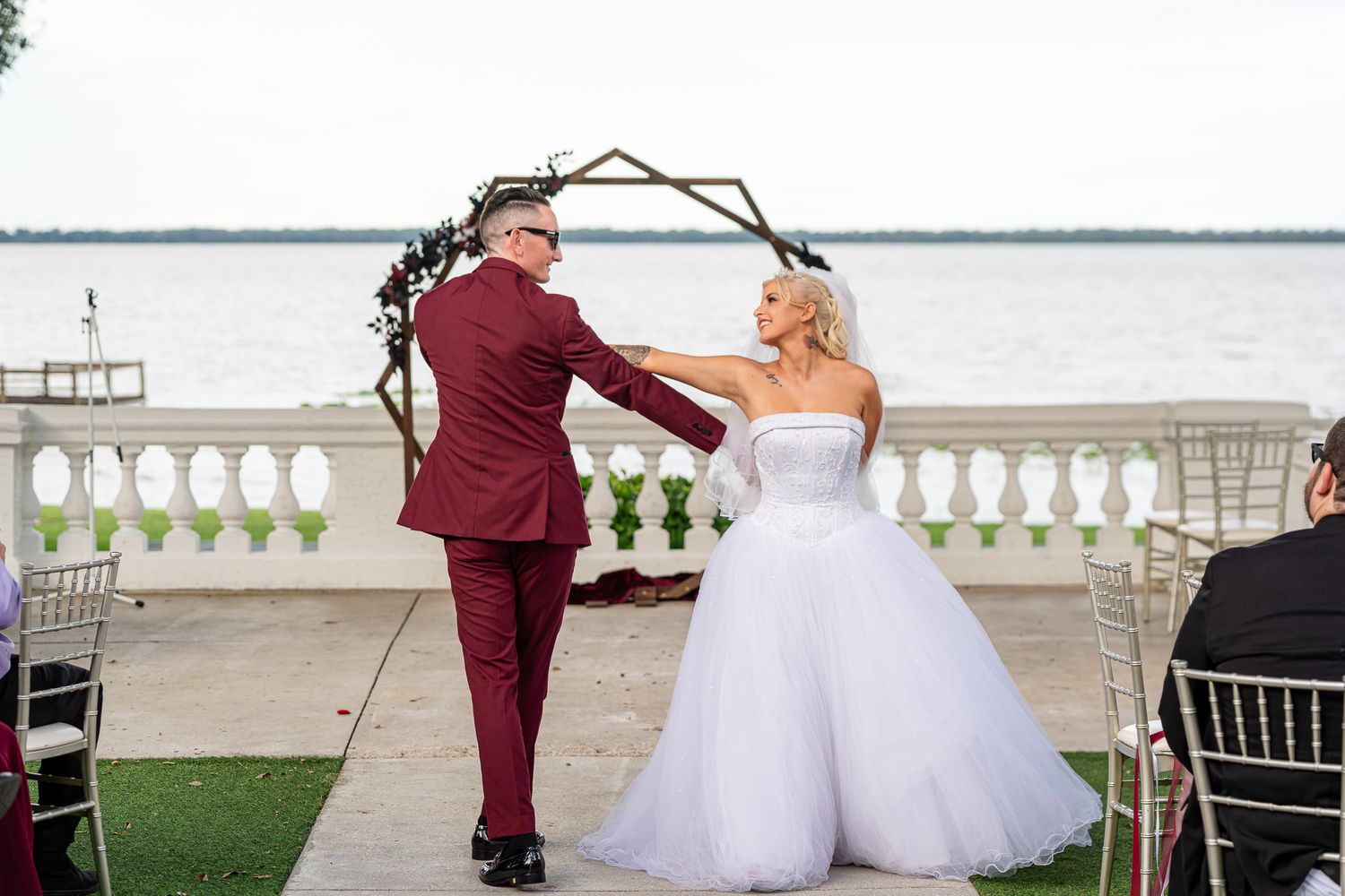 Bride and groom sharing tender moment at outdoor waterfront ceremony under geometric floral arch.