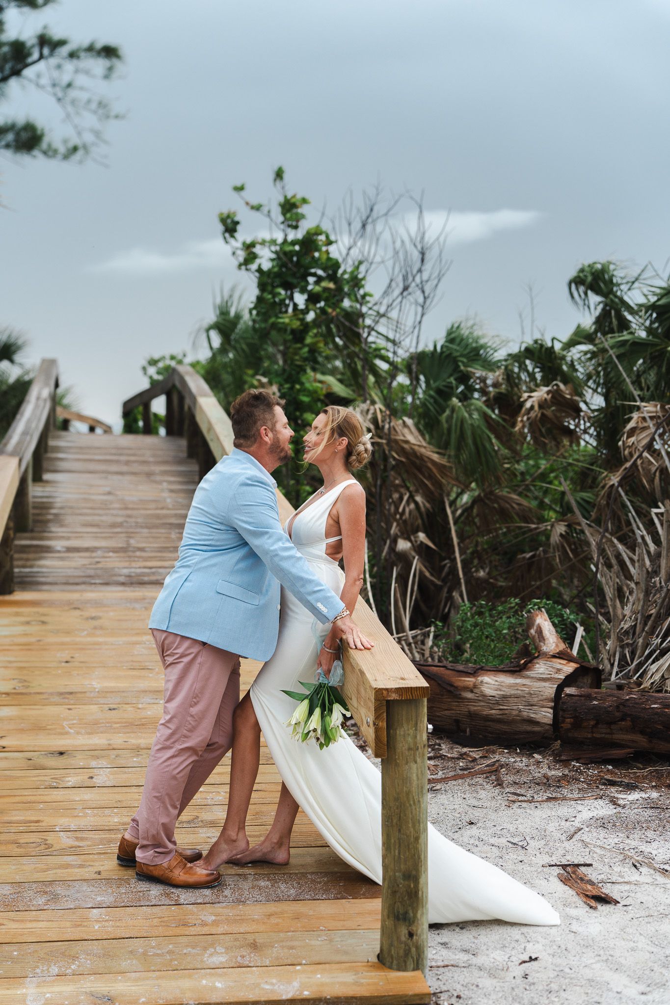 Bride and groom sharing a romantic moment on a wooden boardwalk surrounded by tropical greenery.