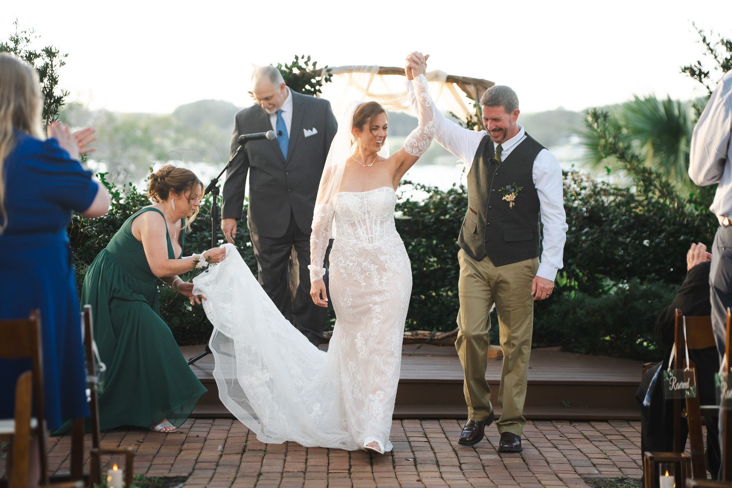 Newlyweds celebrate recessional under raised arch at outdoor wedding ceremony by the water.