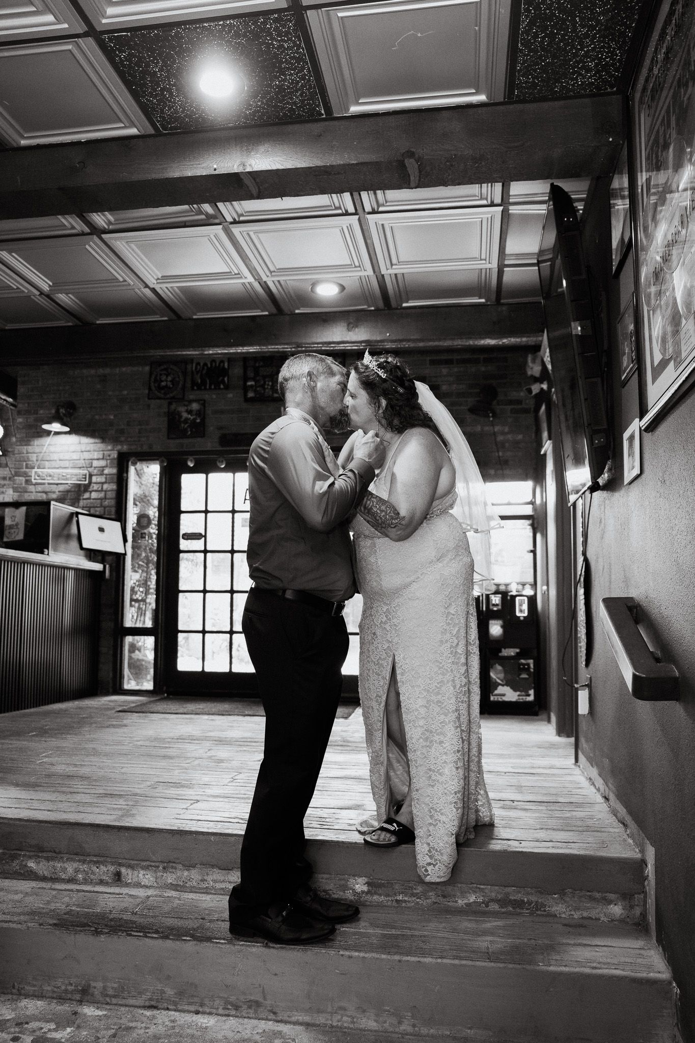 Black and white photo of a bride and groom sharing a tender moment in a rustic indoor venue on their wedding day.