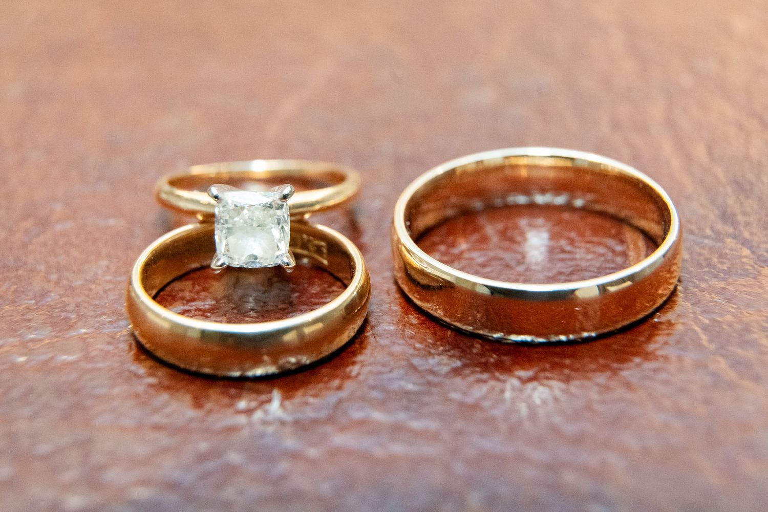 Three gold wedding rings including diamond engagement ring set on rustic brown leather surface.